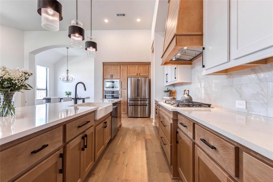 Spacious kitchen with a large island, elegant pendant lighting, and a mix of wood and white cabinetry. It features stainless steel appliances, a stylish range hood, and a bright, airy feel with plenty of natural light. Spacious kitchen with a large island, elegant pendant lighting, and a mix of wood and white cabinetry. It features stainless steel appliances, a stylish range hood, and a bright, airy feel with plenty of natural light.
