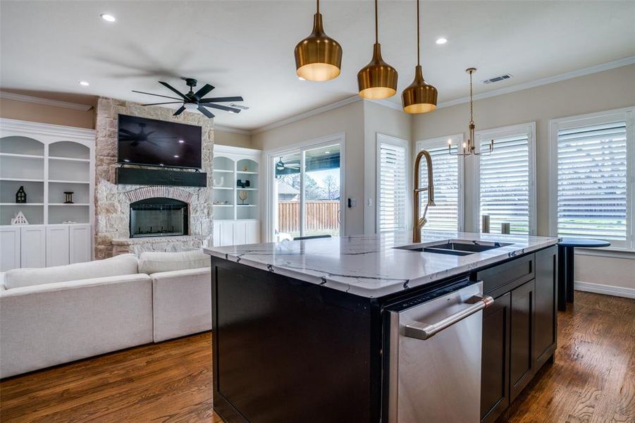 Kitchen featuring light stone counters, pendant lighting, a fireplace, dark hardwood / wood-style floors, and an island with sink