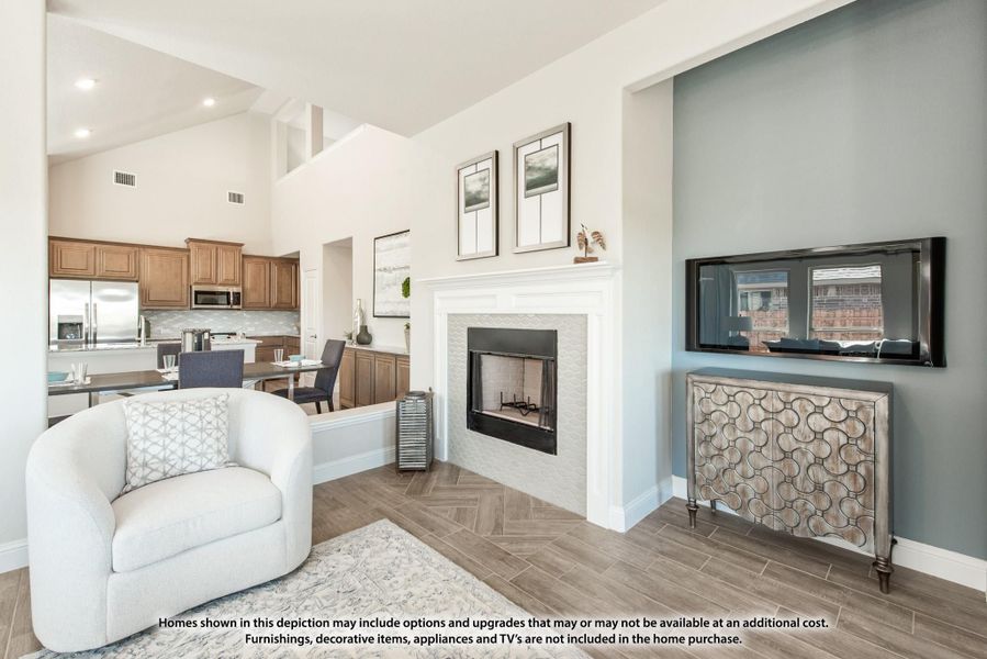 Open-concept living room with white fireplace, wall-mounted TV, and kitchen visible in background with wood cabinets. Open-concept living room with white fireplace, wall-mounted TV, and kitchen visible in background with wood cabinets.