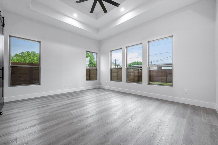 Room with a raised ceiling, ceiling fan, abundant natural light, wood-finished floors, and recessed lighting. Room with a raised ceiling, ceiling fan, abundant natural light, wood-finished floors, and recessed lighting.
