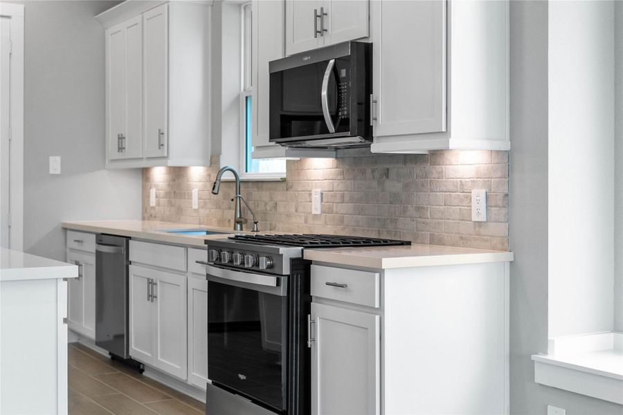 Showcased here is a Whirlpool gas range, paired with a steam microwave equipped with sensor cooking—all framed by an elegant tile backsplash.