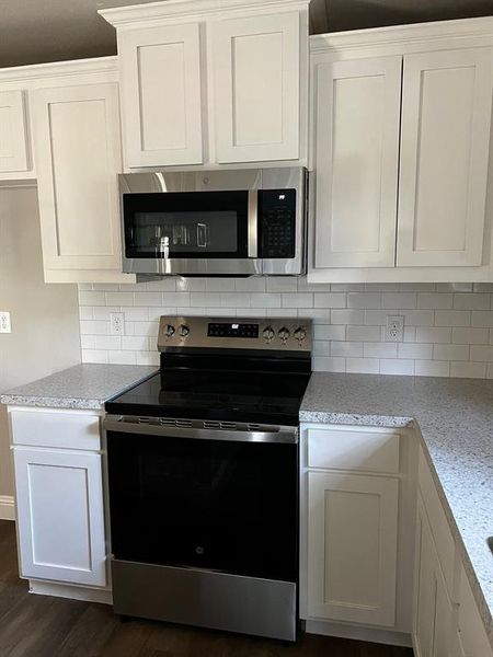 Kitchen featuring white cabinetry, light stone countertops, dark wood-type flooring, and stainless steel appliances