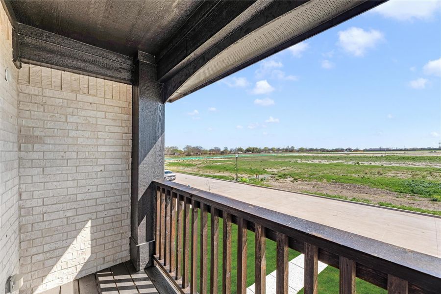 Covered balcony with wood railing and open field views under a blue sky Covered balcony with wood railing and open field views under a blue sky