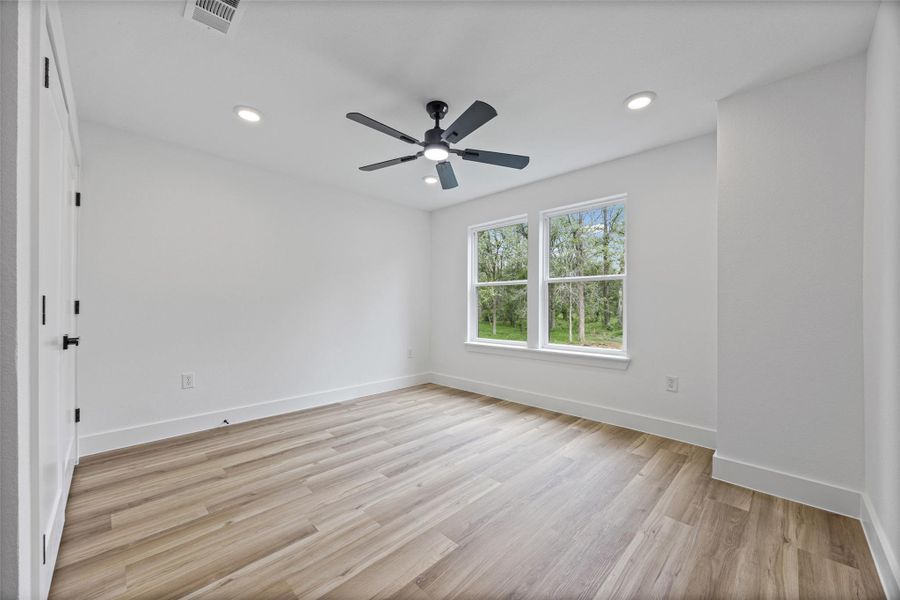 Light-filled bedroom featuring wood-finish flooring and a contemporary ceiling fan with integrated lighting Light-filled bedroom featuring wood-finish flooring and a contemporary ceiling fan with integrated lighting