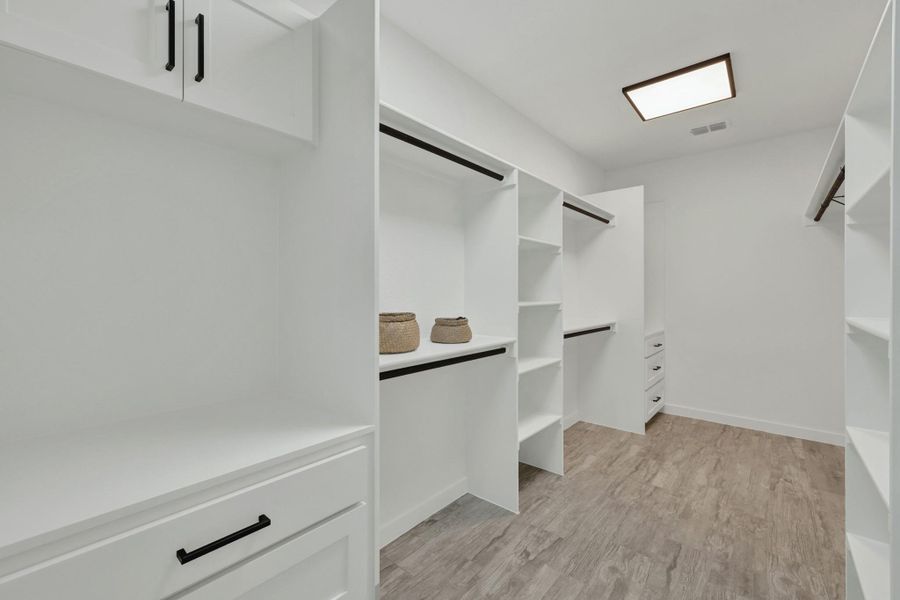 Expansive Master walk-in closet featuring custom white cabinetry with matte black hardware, multiple hanging rods, integrated shelving, and wood-finish flooring