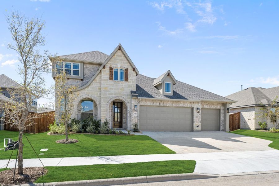 Two-story home with brick and stone exterior, three-car garage, arched entry, and green front lawn