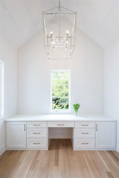 Unfurnished office featuring vaulted ceiling, built in desk, a chandelier, and light hardwood / wood-style flooring