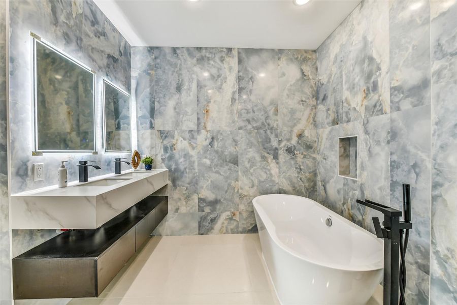 A private spa experience awaits in the first-floor primary suite. A freestanding tub, glass shower, dual sinks, illuminated mirrors and designer tile create a serene start and finish to every day. A private spa experience awaits in the first-floor primary suite. A freestanding tub, glass shower, dual sinks, illuminated mirrors and designer tile create a serene start and finish to every day.