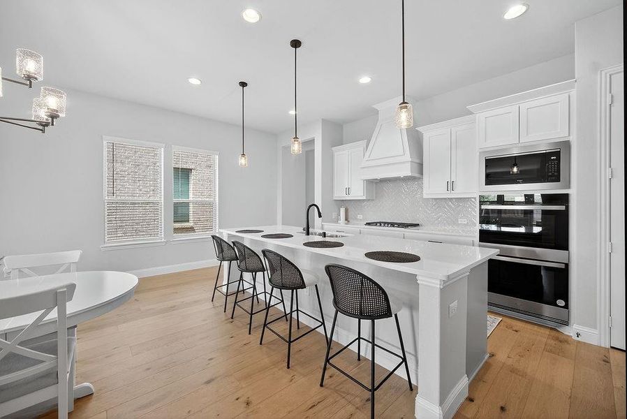 Open-concept kitchen featuring an oversized island with seating, white shaker cabinetry, stainless steel appliances, a range hood, and wood-finish flooring