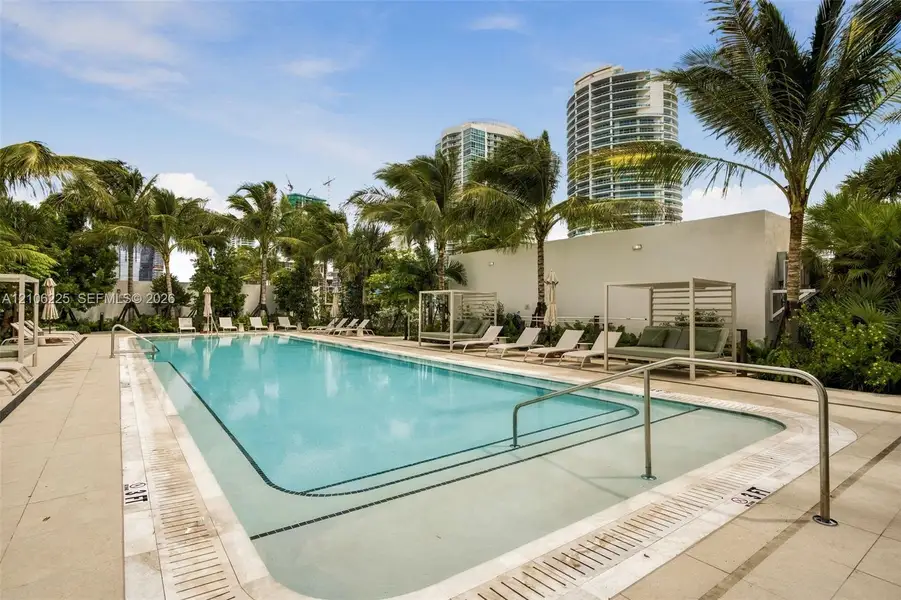 Swimming pool featuring a concrete deck, submerged entry steps, metal handrails, and surrounding palm trees Swimming pool featuring a concrete deck, submerged entry steps, metal handrails, and surrounding palm trees