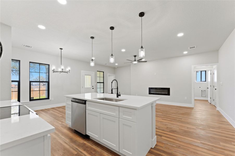 Kitchen featuring a glass covered fireplace, open floor plan, white cabinetry, light stone countertops, and a center island with sink