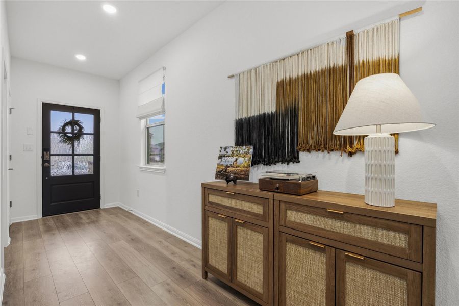 Entryway featuring wood-finish flooring, a black paneled door with glass inserts, recessed lighting, and a window with a Roman shade