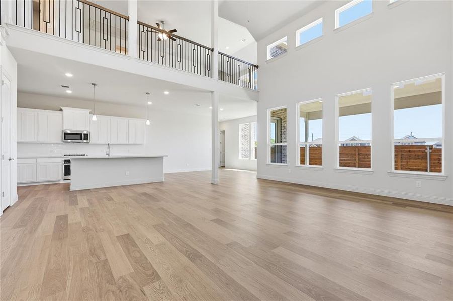 Unfurnished living room with a ceiling fan, light wood finished floors, recessed lighting, and a high ceiling