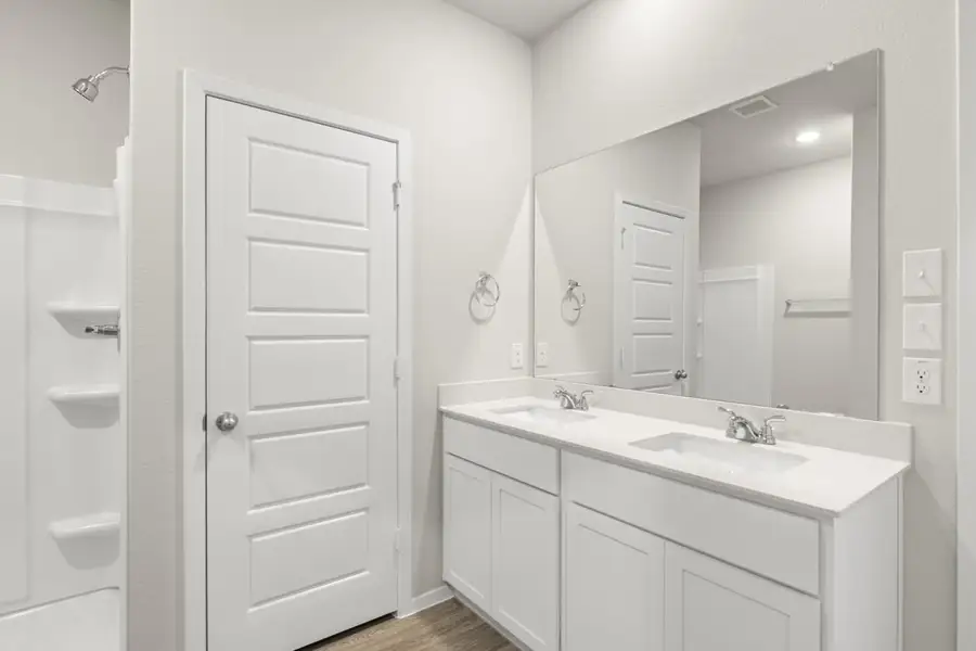Image of a primary bathroom with light grey walls, a white jack and jill vanity, a large mirror and a white standing shower Image of a primary bathroom with light grey walls, a white jack and jill vanity, a large mirror and a white standing shower