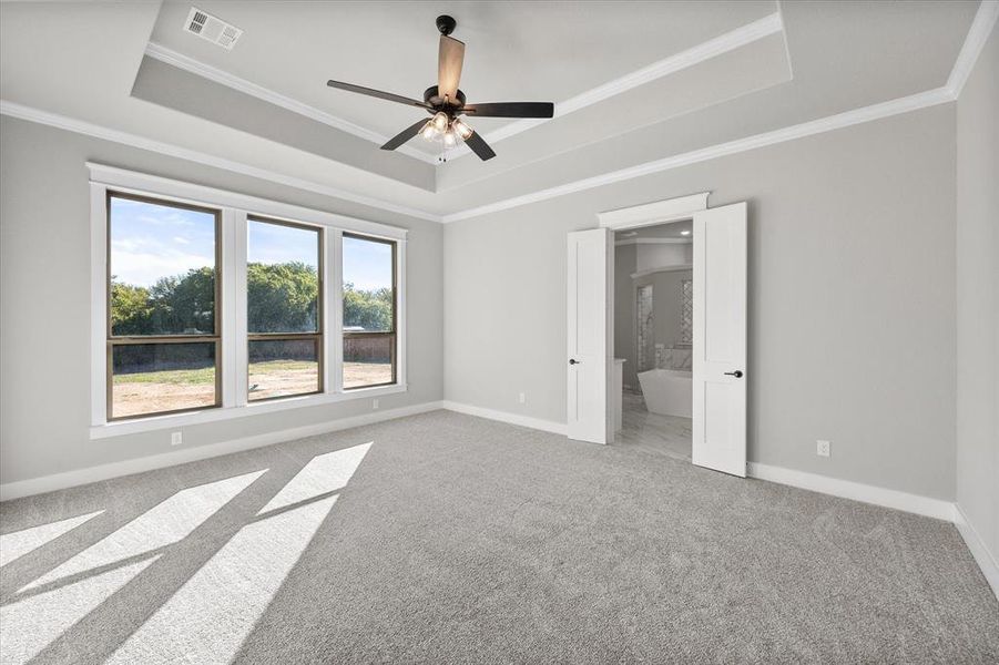 Primary suite with tray ceiling and crown molding. French doors to en-suite bathroom.