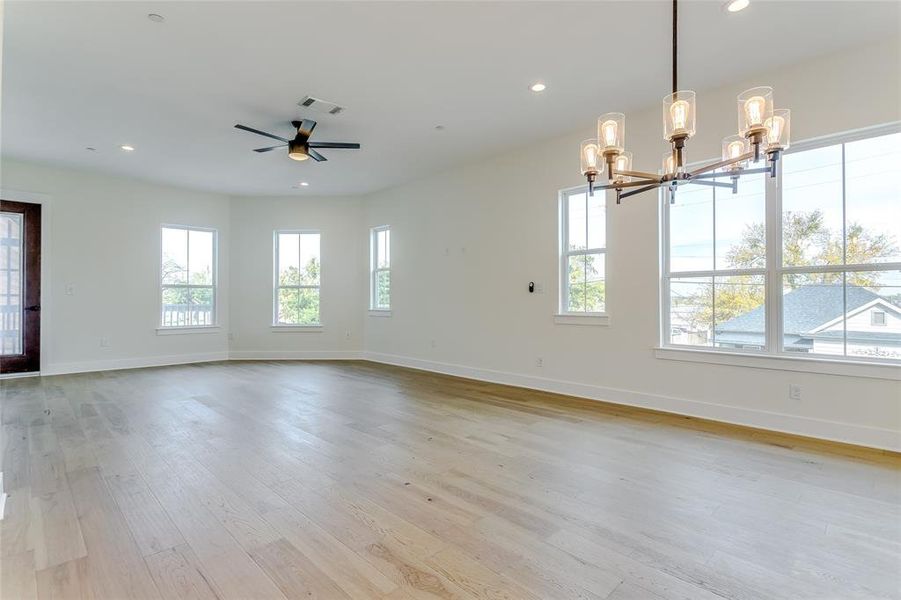 Unfurnished room with ceiling fan with notable chandelier, light hardwood / wood-style flooring, and plenty of natural light