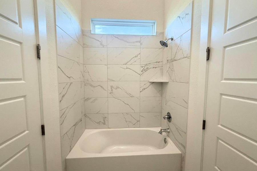 Bathtub shower with white marble-look wall tiling, a built-in shelf, and a transom window