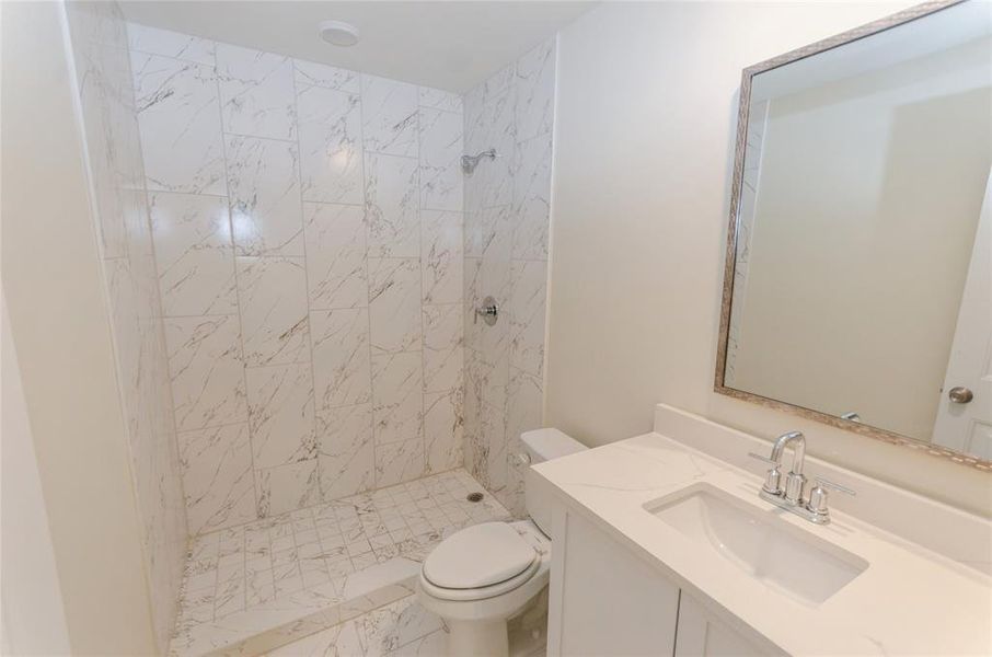 Bathroom with a tile shower, vanity, and toilet