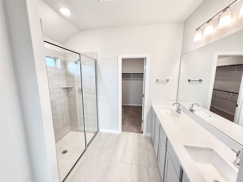 Full bath featuring a spacious closet, a stall shower, double vanity, light tile patterned floors, and vaulted ceiling Full bath featuring a spacious closet, a stall shower, double vanity, light tile patterned floors, and vaulted ceiling