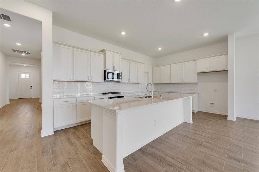 Kitchen featuring white cabinets, backsplash, sink, and a center island with sink