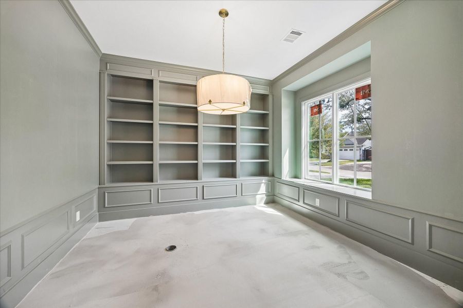 Dedicated study with custom built in shelving and detailed millwork creates a refined and functional work from home space. Soft natural light pours in through the oversized window, highlighting the elegant wall paneling and designer lighting overhead. The thoughtfully designed built ins provide ample storage and display space, while the neutral color palette offers a calm and sophisticated environment ideal for productivity or a quiet reading retreat.