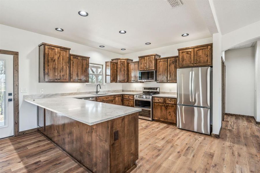 Kitchen featuring visible vents, light wood-style flooring, a peninsula, appliances with stainless steel finishes, and a sink