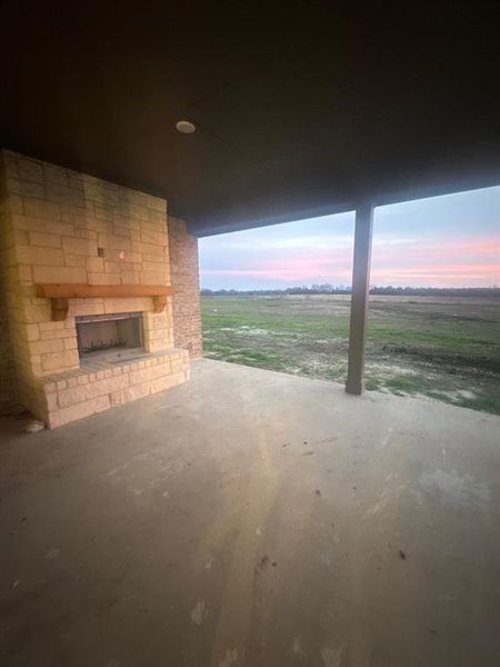 Patio terrace at dusk featuring an outdoor stone fireplace, a patio, and a view of rural / pastoral area