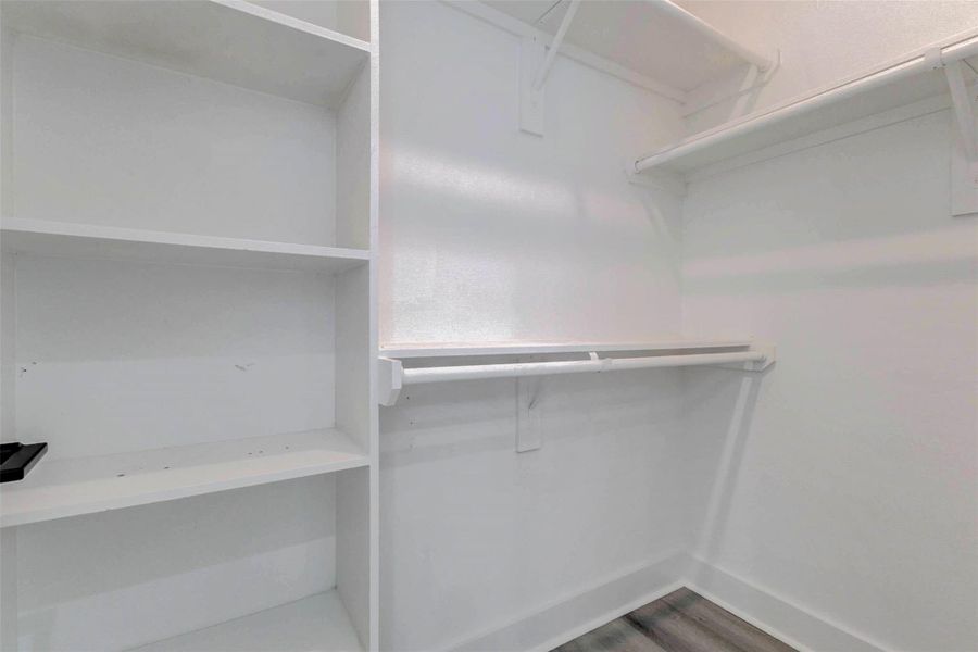 The walk-in closet offers practical organization with multiple hanging rods, upper shelving, and built-in open storage. Its spacious layout provides room for clothing, shoes, accessories, and seasonal items, while the neutral white finish and plank flooring create a clean, streamlined appearance. The walk-in closet offers practical organization with multiple hanging rods, upper shelving, and built-in open storage. Its spacious layout provides room for clothing, shoes, accessories, and seasonal items, while the neutral white finish and plank flooring create a clean, streamlined appearance.