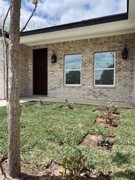 Doorway to property featuring a lawn, covered porch, and brick siding Doorway to property featuring a lawn, covered porch, and brick siding