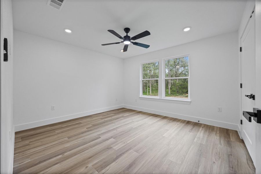 Room featuring wood-finish flooring, a modern black ceiling fan, recessed lighting, and two windows providing exterior views Room featuring wood-finish flooring, a modern black ceiling fan, recessed lighting, and two windows providing exterior views
