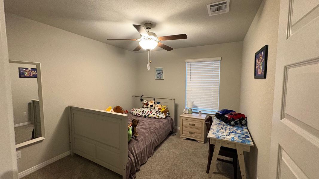 An inviting bedroom with plush carpeting and a modern ceiling fan for year-round comfort.