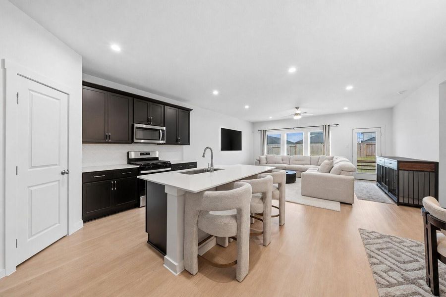 The open-concept design effortlessly blends the kitchen and living spaces, highlighted by a large island with seating, sleek dark cabinetry, and a wall of windows that brings in abundant natural light.