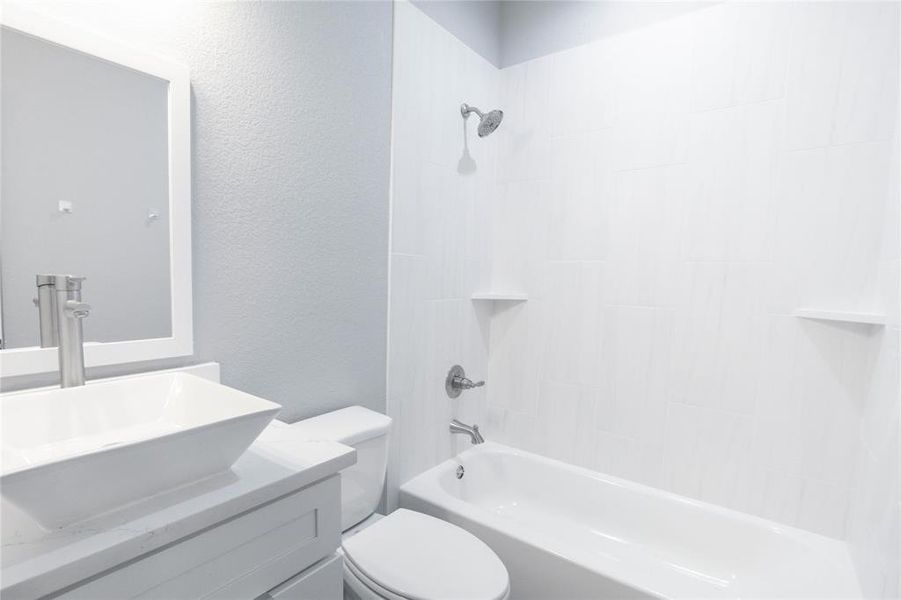 Full bath featuring washtub / shower combination, vanity, and a textured wall