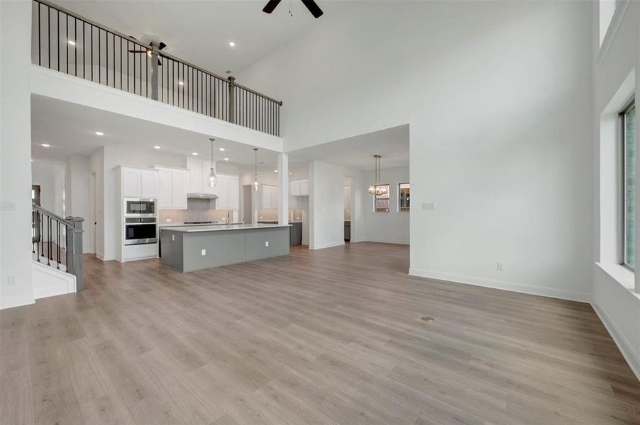 Open-concept interior featuring high ceilings, wood-finish flooring, a contemporary kitchen with white cabinetry and a gray island, and a second-story balcony overlooking the main living area Open-concept interior featuring high ceilings, wood-finish flooring, a contemporary kitchen with white cabinetry and a gray island, and a second-story balcony overlooking the main living area