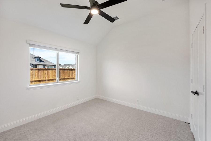 Empty bedroom with vaulted ceiling, black ceiling fan, carpet flooring, and a window overlooking a wood fence. Empty bedroom with vaulted ceiling, black ceiling fan, carpet flooring, and a window overlooking a wood fence.