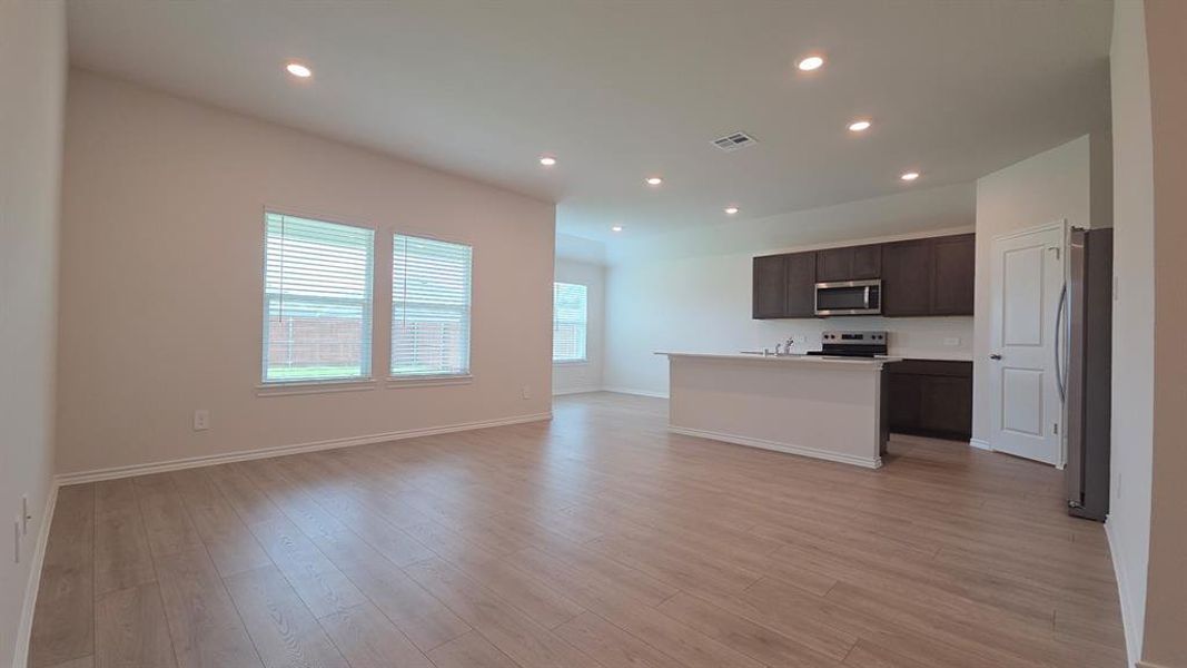 Open-concept living area featuring wood-finish flooring, recessed lighting, and multiple windows with blinds Open-concept living area featuring wood-finish flooring, recessed lighting, and multiple windows with blinds