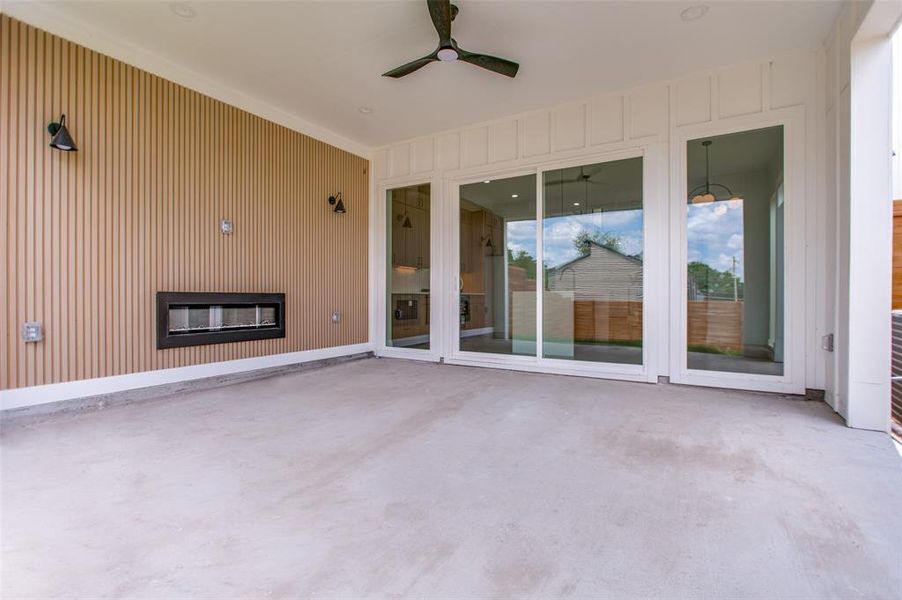 Covered outdoor patio featuring a linear built-in fireplace, slatted accent wall, and a ceiling fan