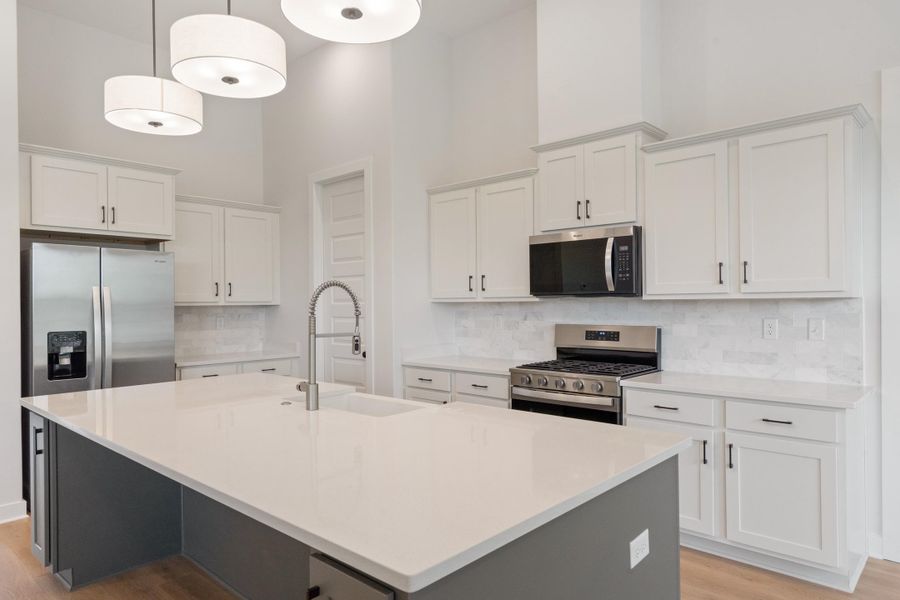 Open-concept kitchen featuring an expansive island with an undermount sink, white shaker cabinetry, stainless steel appliances, and a tile backsplash