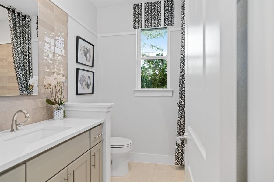 Bathroom with vanity, decorative backsplash, and tile patterned floors. The photos shown are of a completed home with the same floor plan and may not reflect the exact finishes, features, or layout of the home currently under construction.