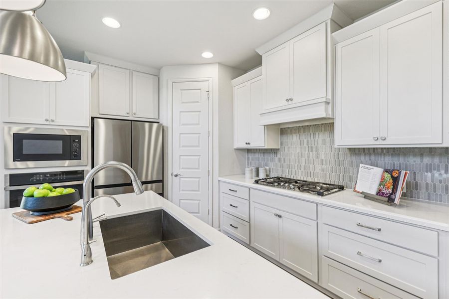 The kitchen features white cabinetry, stainless steel appliances, a gas cooktop, and a large kitchen island with an undermount sink