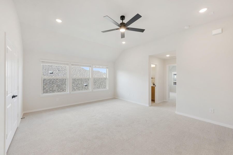 Empty bedroom with vaulted ceiling, ceiling fan, carpet flooring, and ensuite bathroom entrance