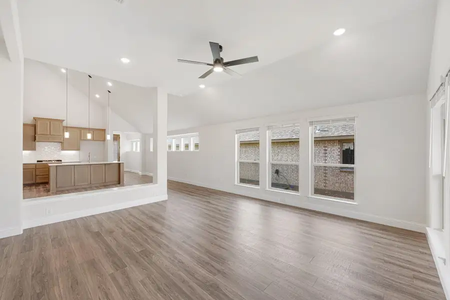 Open living room with hardwood floors and ceiling fan, open to kitchen with wood cabinets and vaulted ceiling