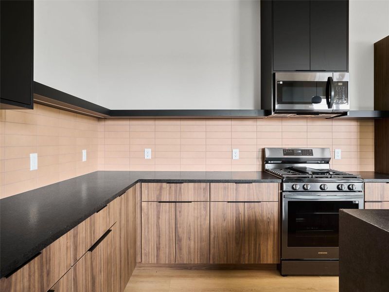 Kitchen featuring stainless steel appliances, backsplash, modern cabinets, and dark stone countertops Kitchen featuring stainless steel appliances, backsplash, modern cabinets, and dark stone countertops