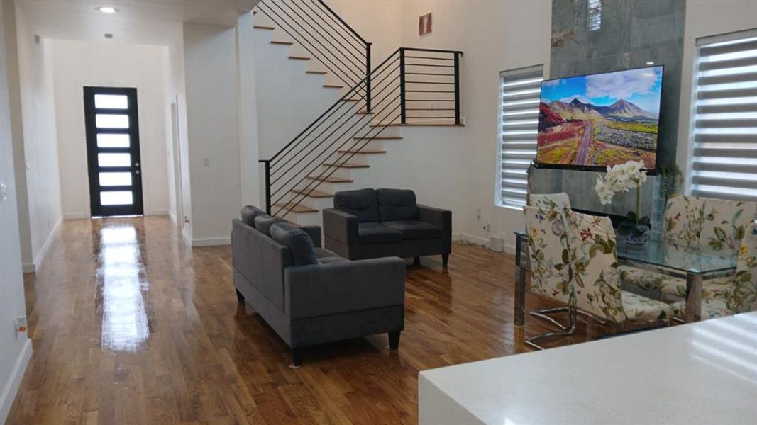 Open-concept living area featuring wood-finish flooring, a contemporary staircase with horizontal railings, and a statement accent wall with integrated media space