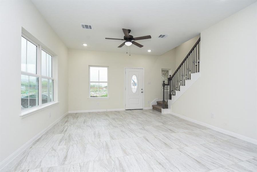 Empty living space with tiled floor, staircase, ceiling fan, and windows, in a new house.