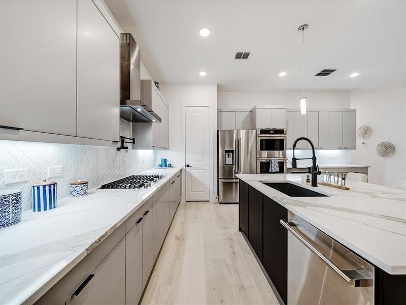 Kitchen with modern cabinets, appliances with stainless steel finishes, light stone countertops, hanging light fixtures, and recessed lighting Kitchen with modern cabinets, appliances with stainless steel finishes, light stone countertops, hanging light fixtures, and recessed lighting