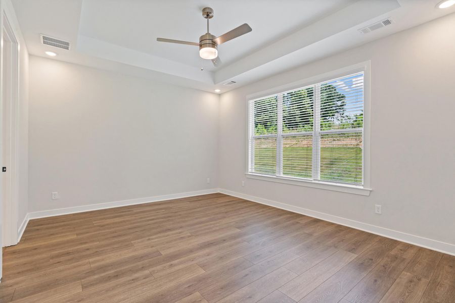 Spacious room featuring wood-finish flooring, a tray ceiling with recessed lighting, an overhead ceiling fan, and a large window with blinds Spacious room featuring wood-finish flooring, a tray ceiling with recessed lighting, an overhead ceiling fan, and a large window with blinds