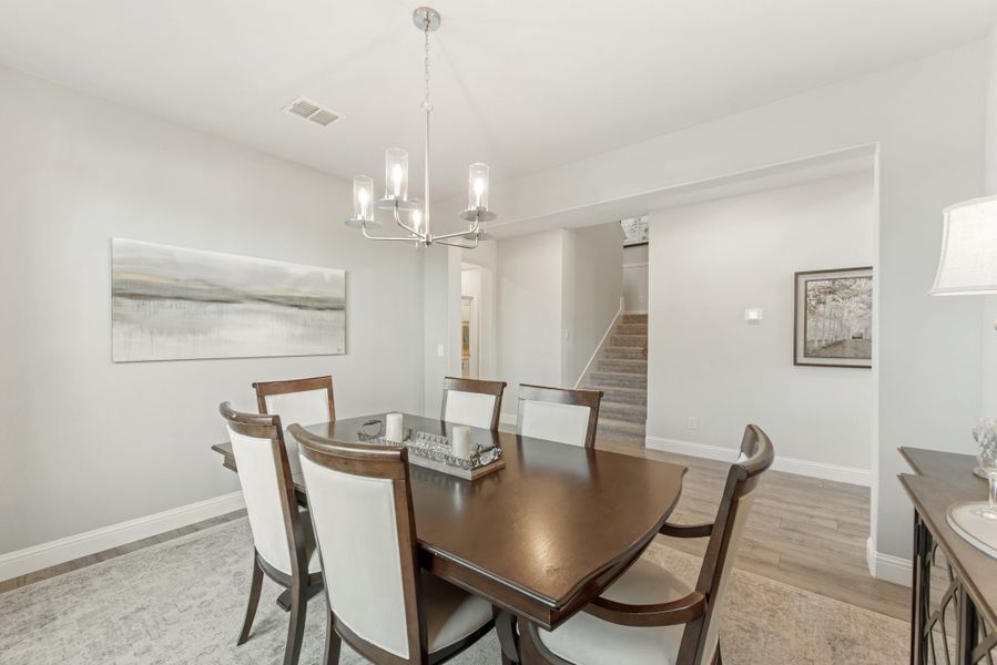 Dining room with dark wood table, six chairs, and a chandelier above on light hardwood floors