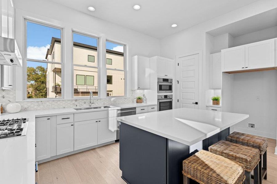 Kitchen featuring white cabinets, light wood finished floors, tasteful backsplash, a kitchen breakfast bar, and recessed lighting Kitchen featuring white cabinets, light wood finished floors, tasteful backsplash, a kitchen breakfast bar, and recessed lighting