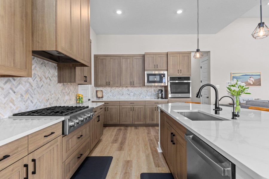 Kitchen with premium range hood, appliances with stainless steel finishes, light wood finished floors, and pendant lighting